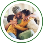 A grandmother hugs her two grandchildren with both arms while they all smile broadly. 